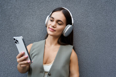 A young brunette woman with a joyful smile listens to music outdoors, fully immersed in her moment of leisure and relaxation.の写真素材