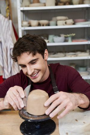 Sophisticated merry man in apron making some pottery in studio.の写真素材