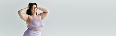 A confident plus size woman radiates joy while playfully posing with her hands in her hair.の写真素材