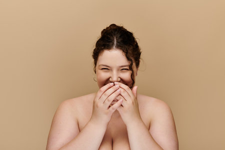 A beautiful plus size woman joyfully covers her mouth, radiating confidence and charm.の写真素材