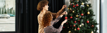 Two young professionals happily adorn a Christmas tree with ornaments in their workspace.の写真素材
