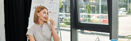 Woman enjoys a snack in a modern office filled with natural light.の写真素材