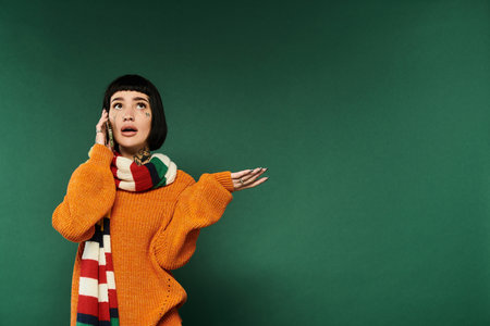 The young woman expresses herself while relaxed in a warm sweater, surrounded by a vibrant green backdrop.の写真素材