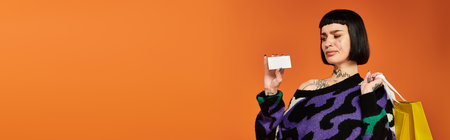 A young woman with short hair and tattoos poses confidently in a vibrant sweater against a bold orange backdrop.の写真素材