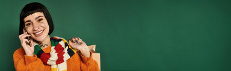 A young woman in a colorful sweater poses playfully, showcasing her tattoos and bright smile in a...