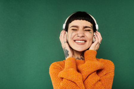 A young woman with short hair and tattoos smiles brightly while wearing a cozy sweater in a warm studio.の写真素材