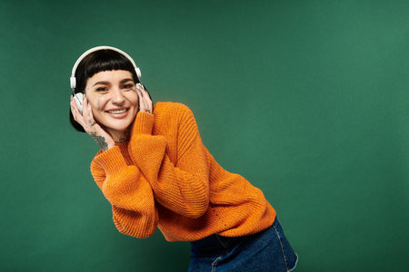 A cheerful young woman with tattoos enjoys her time in a warm sweater, posing playfully in a studio setting.の写真素材