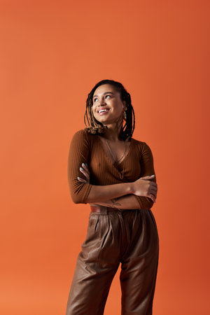A fashionable young woman with braided hair stands with arms crossed, smiling brightly against an...