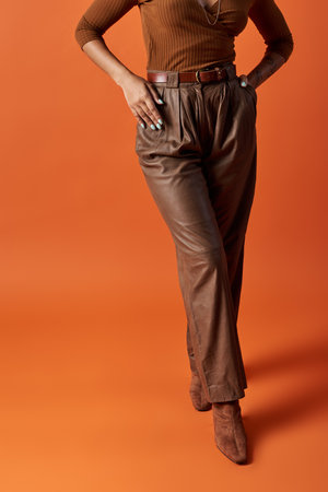 A young, fashion-forward woman showcases her stylish outfit against a striking orange backdrop.