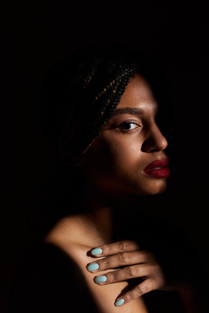 A stylish young woman flaunts her braids and bold red lips in a dramatic studio setting.