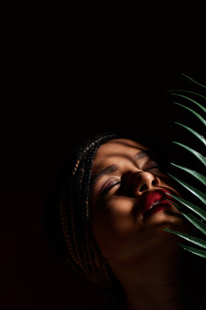 A young woman with braided hair displays vibrant red lips while posing gracefully in a studio.の写真素材