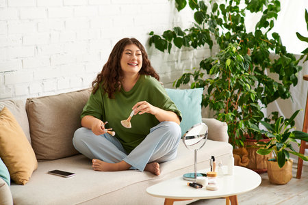 A young curly woman relaxes on the couch, happily engaging in her beauty routine with makeup products.の写真素材