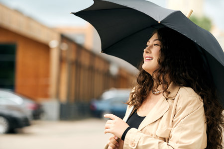 A young woman in a stylish black dress and trench coat smiles while enjoying a vibrant autumn day outside.の写真素材