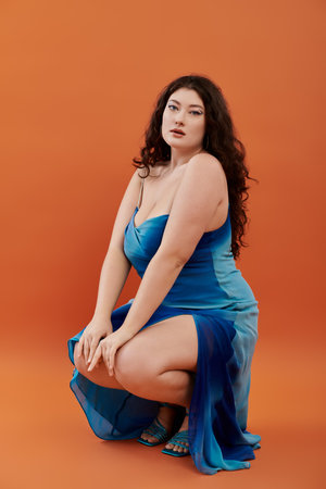 A young, beautiful plus size woman showcases a stunning blue dress while confidently posing in a studio setting.の写真素材