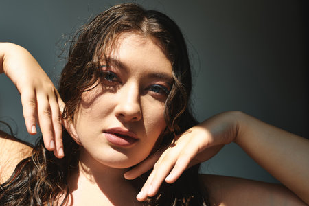 A stunning plus-size woman confidently poses against a  grey backdrop.