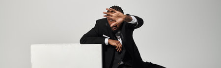 A young man in a well-fitted suit poses confidently against a grey backdrop, showcasing elegance and...