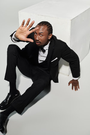 A young man dressed elegantly in a suit strikes a unique pose against a grey background, showcasing confidence.の写真素材