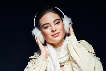 A woman embraces the winter season with fashionable earmuffs and a warm scarf, smiling warmly.の写真素材
