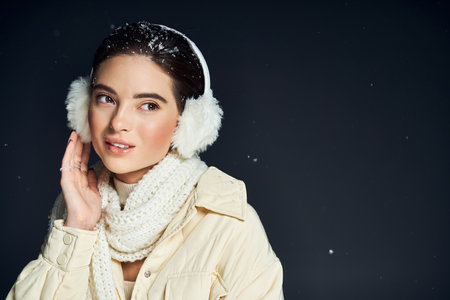 A joyful woman wearing earmuffs and a cozy scarf smiles as snowflakes gently fall around her.の写真素材