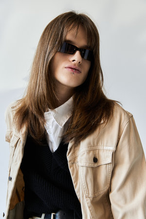 A stylish young guy stands confidently, adorned in trendy attire and modern sunglasses.
