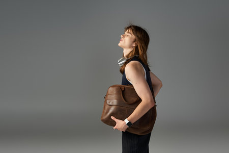A young man showcases modern fashion with a brown bag, exuding confidence in a stylish outfit.の写真素材