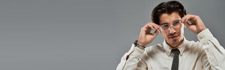 The young man adjusts his glasses with a charming smile, showcasing his formal look against a muted backdrop.の写真素材