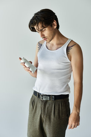 A young, handsome man with a tattoo examines a self-care product while dressed casually against a grey backdrop.の写真素材