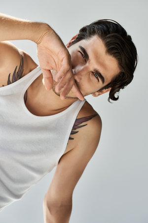 A young man showcases his tattoos while striking a confident pose in a fitted tank top, creating a bold aesthetic.の写真素材