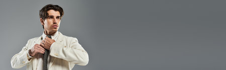 A young man adjusts his tie in a stylish formal outfit, exuding confidence in a chic studio setting.の写真素材