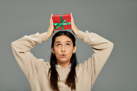 A young woman with emotional expression delights in holding a red gift wrapped in green ribbon.の写真素材