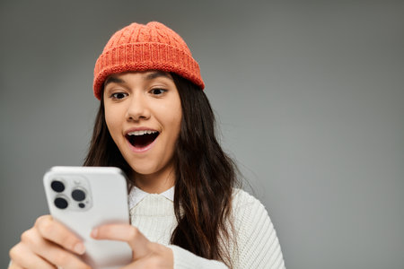 A young woman excitedly interacts with her smartphone, showing off her stylish outfit.の写真素材