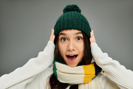 A young woman in a cozy hat and scarf expresses excitement with a surprised look.