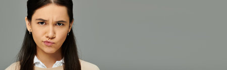 A young woman conveys deep emotions in a modern, stylish outfit against a simple background.