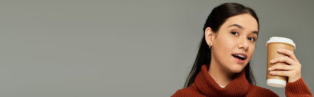 A young woman dressed in fashionably cozy attire enjoys her coffee with a joyful expression.