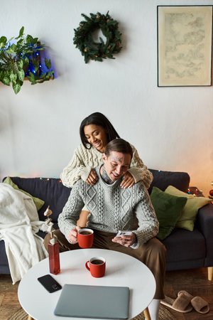 A loving couple enjoys time together at home, celebrating Christmas with cozy drinks and joy.の写真素材
