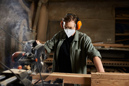 A dedicated carpenter engages with a saw, meticulously crafting wood in her vibrant workshop.の写真素材