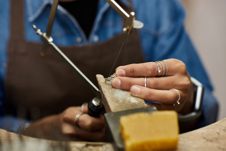 A skilled artisan expertly shapes fine jewelry with meticulous attention in a warm workshop.の写真素材