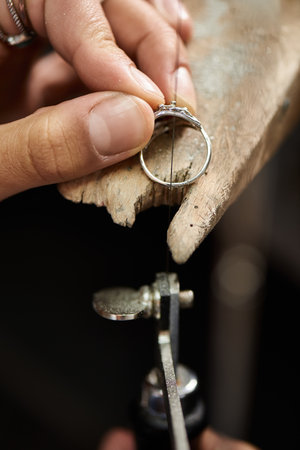 Craftsmanship shines as hands work meticulously on a sparkling ring set in a workshop.の写真素材