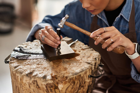 A talented craftswoman delicately hammers metal on a wooden block, showcasing her artistry.の写真素材