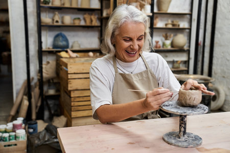 A happy woman creates pottery, focusing intently on her artwork in a lively workshop.の写真素材