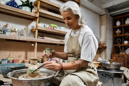 A skilled mature woman carefully crafts pottery while enjoying her creative process.の写真素材