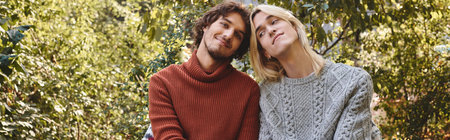Young loving gay couple share a joyful moment in a vibrant garden. Dressed in cozy sweaters, they...