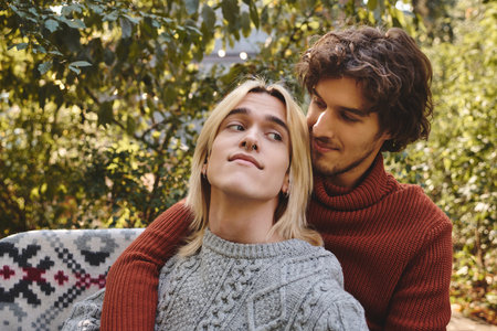 Two young men share a sweet and intimate embrace while surrounded by lush greenery. Their expressions reflect joy and love, highlighting a serene day outdoors.の写真素材