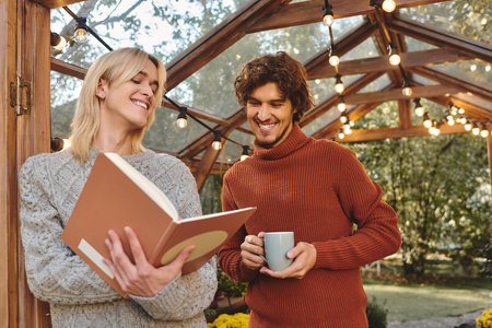 Young loving gay couple smile as they engage with a book in a charming outdoor space adorned with lights. The atmosphere radiates warmth and connection as they enjoy each others company.の写真素材