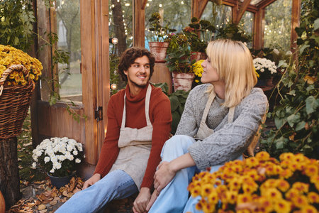 Two handsome young men relax in a lush garden filled with colorful flowers. With smiles on their faces, they share a joyful moment surrounded by natures beauty in a warm autumn afternoon.の写真素材
