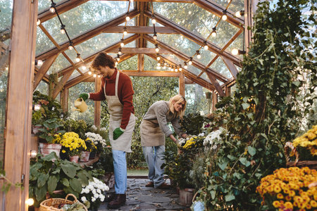 Young loving gay couple enjoy a peaceful afternoon in a beautifully lit greenhouse, surrounded by colorful flowers and greenery, while nurturing their love for gardening together.の写真素材