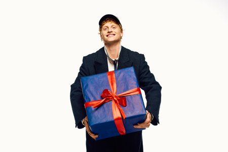 Smiling man dressed in trendy holiday fashion presents a beautifully wrapped gift, capturing the festive spirit of Christmas 2025.の写真素材