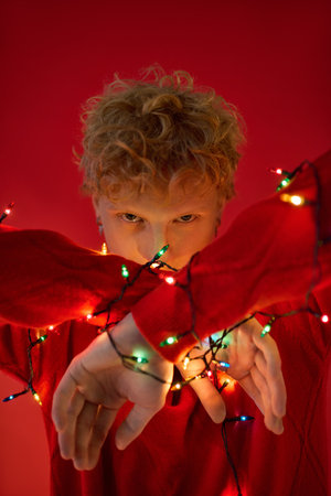 A young man showcases festive holiday fashion with bright Christmas lights wrapped around his arms.の写真素材