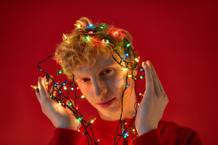 A stylish young man showcases his creativity by wrapping colorful holiday lights around his head.