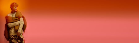 A stylish man showcases holiday fashion with an eye catching outfit, wrapped in cozy layers against a bold orange and pink backdrop, embodying the festive spirit of Christmas 2025.の写真素材